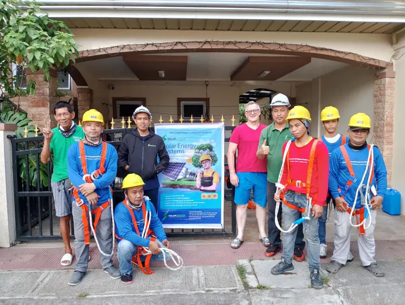 Solar installation team and supervisors posing with safety equipment in front of residential solar energy systems banner