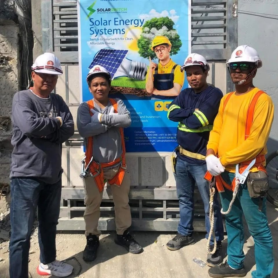Five construction workers in safety gear posing in front of Solar Switch renewable energy billboard
