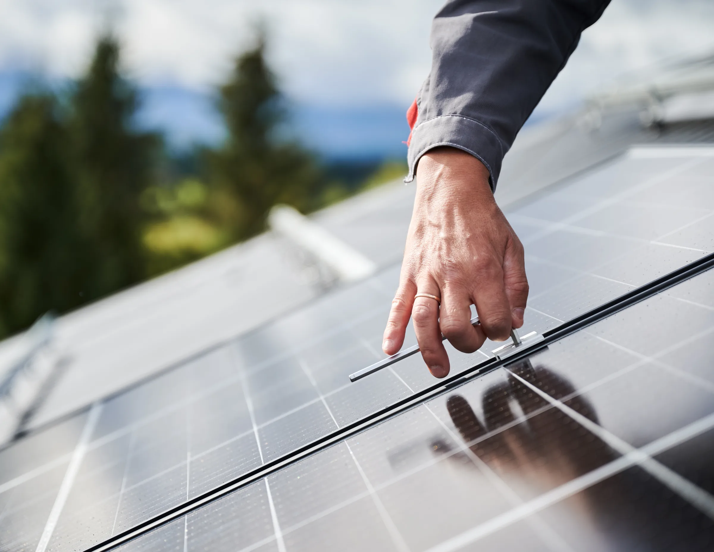 Technician installing solar panel on rooftop with mountains and evergreen trees in background