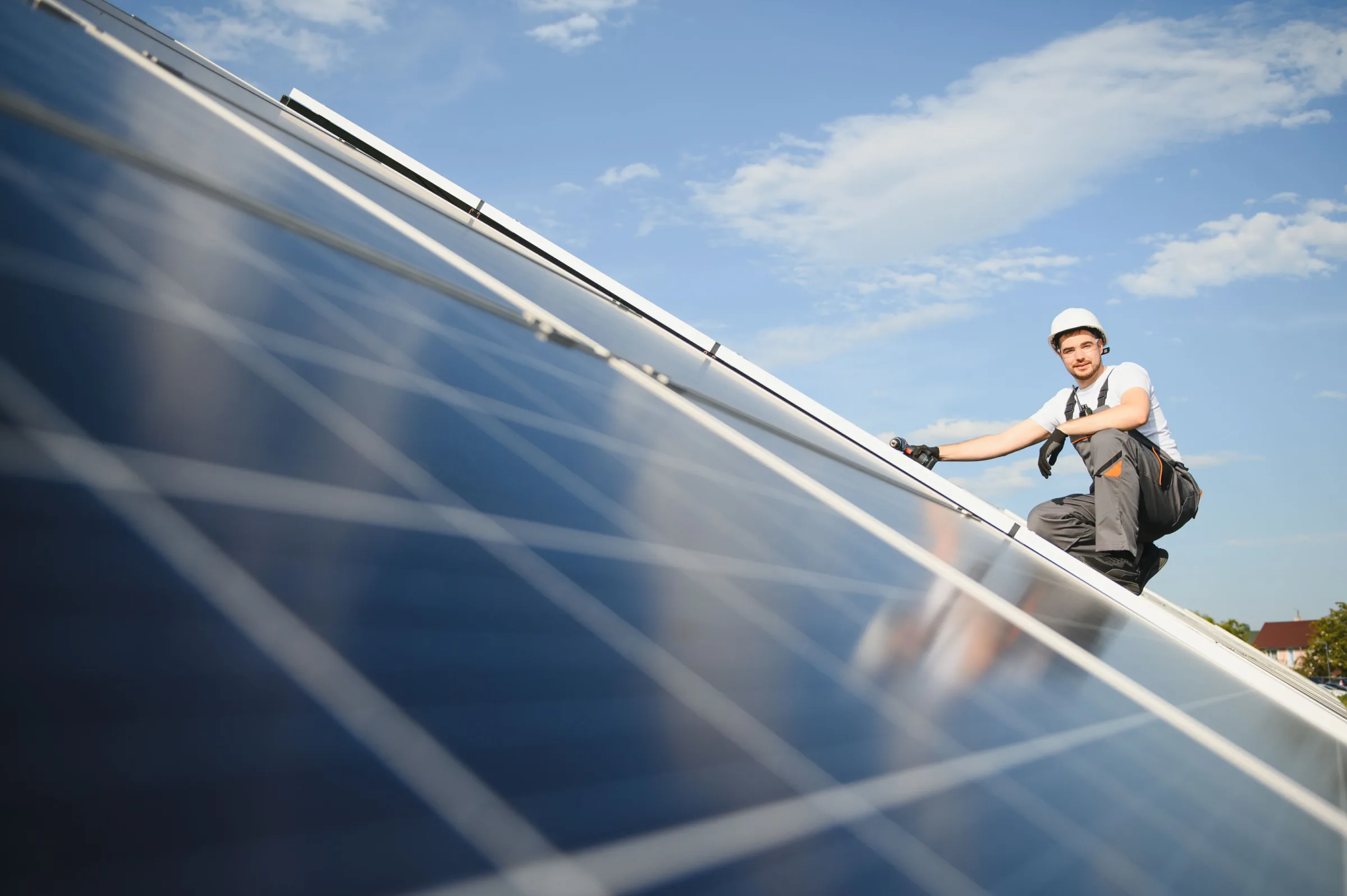 Worker in hard hat installing solar panels on residential rooftop under clear sky
