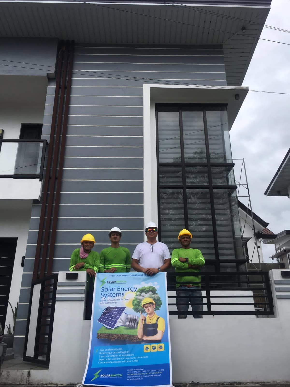 Solar installation team holding Solar Energy Systems banner in front of modern house with solar panels
