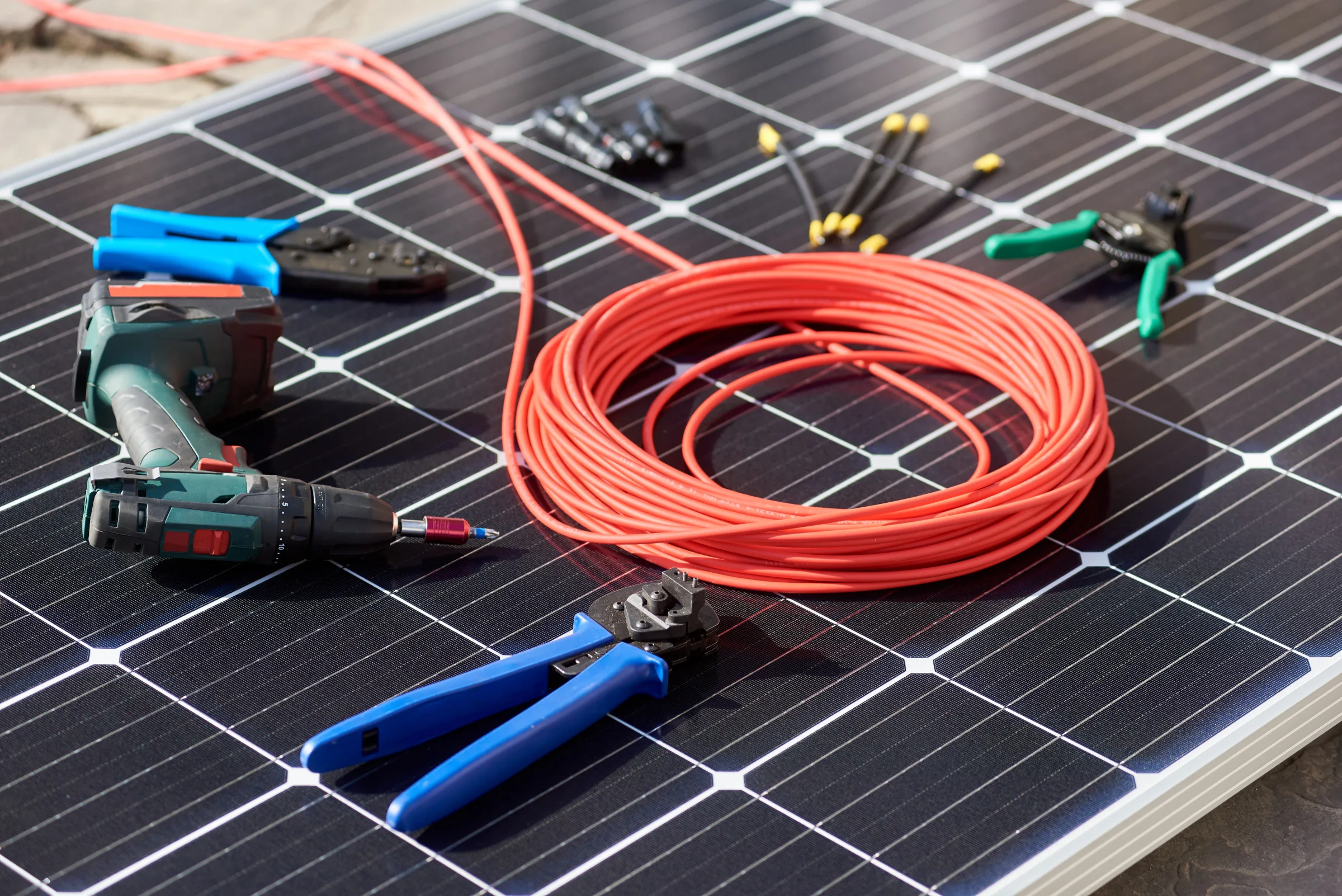 Solar panel installation tools including red cables, blue crimpers, connectors, and wire strippers arranged on a