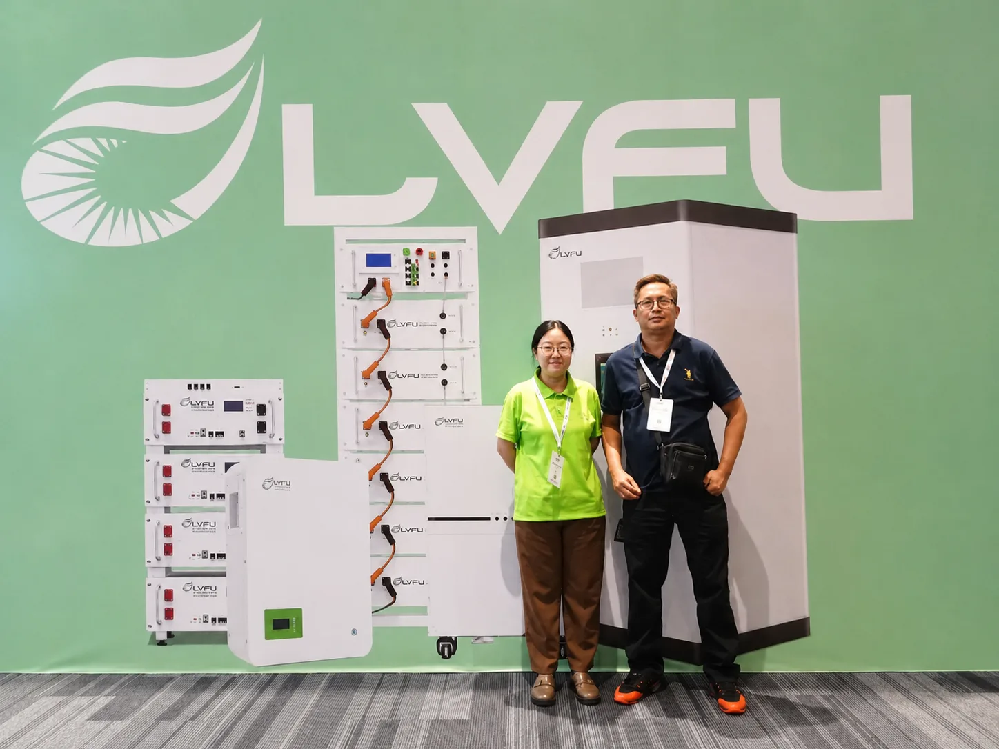 Two people standing in front of LVFU solar energy storage systems and battery equipment display wall